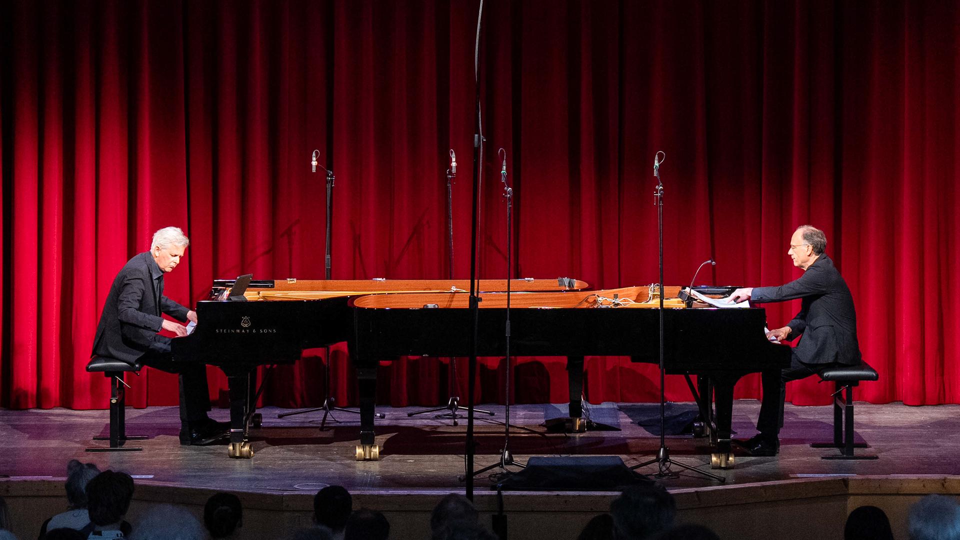 Zwei Pianisten an ihren gegenüberliegenden Instrumenten vor einem roten Vohang auf der Bühne der Rudolf Steiner Schule Zwei Pianisten an ihren gegenüberliegenden Instrumenten vor einem roten Vohang auf der Bühne der Rudolf Steiner Schule