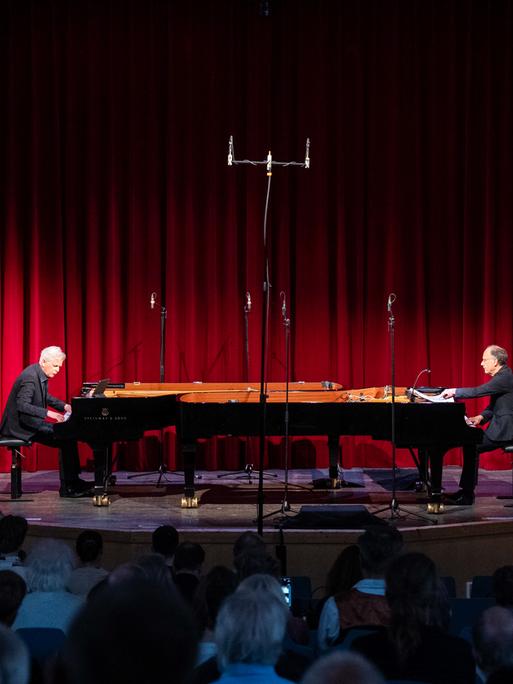 Zwei Pianisten an ihren gegenüberliegenden Instrumenten vor einem roten Vohang auf der Bühne der Rudolf Steiner Schule 