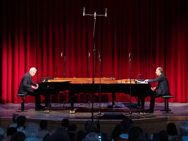 Zwei Pianisten an ihren gegenüberliegenden Instrumenten vor einem roten Vohang auf der Bühne der Rudolf Steiner Schule 