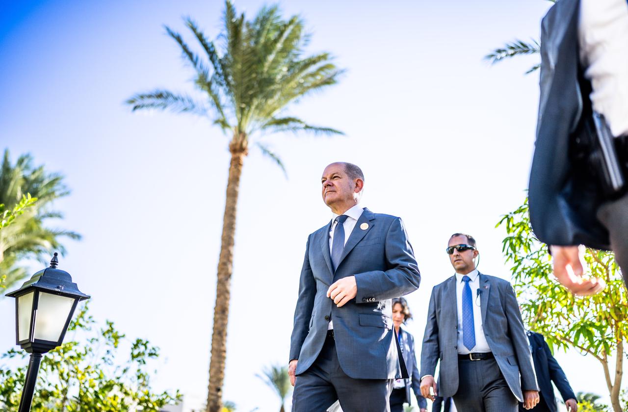 Bundeskanzler Olaf Scholz bei der UN-Weltklimakonferenz in Ägypten an einer Palme vorbei,begleitet von einem Personenschützer.