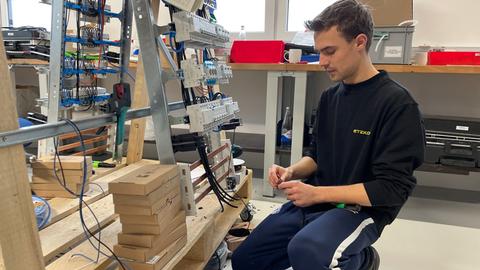 Ein junger Elektrotechniker verrichtet in einer Werkstatt konzentriert seine Arbeit.