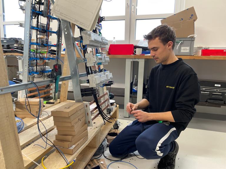 Ein junger Elektrotechniker verrichtet in einer Werkstatt konzentriert seine Arbeit.