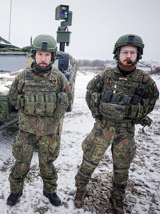 Drei Bundeswehr-Soldaten stehen im Schnee vor einem gepanzerten Fahrzeug.