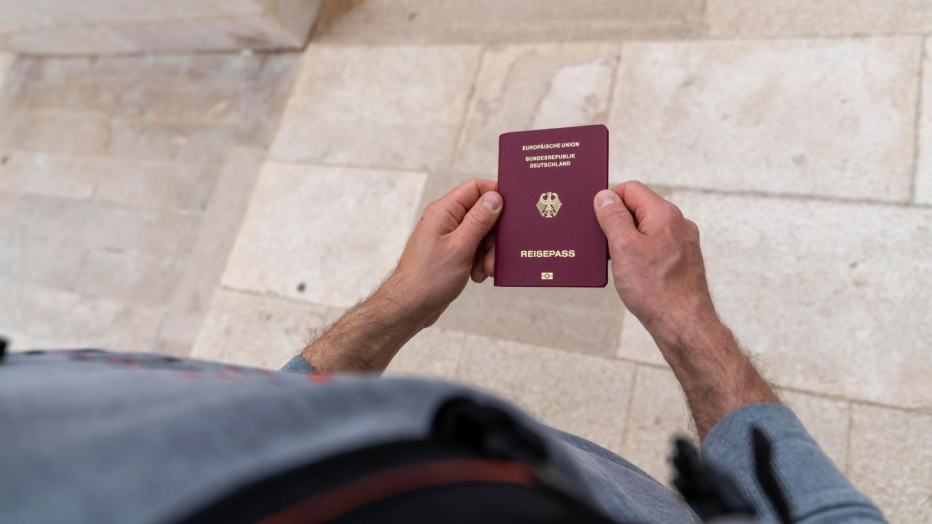 Ein Mann hält einen Deutschen Reisepass in der Hand.