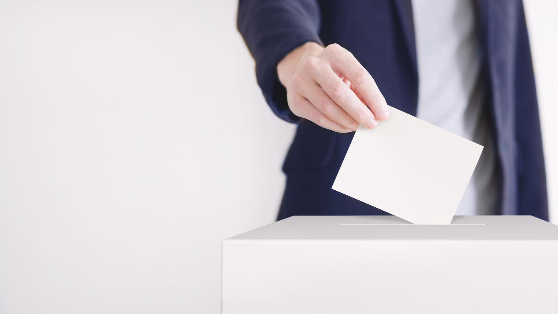 Ein Mann steckt einen Wahlzettel in eine Wahlurne.
