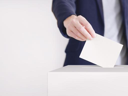 Ein Mann steckt einen Wahlzettel in eine Wahlurne.