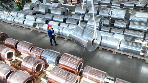 Ein Arbeiter geht durch einen Gang in einer Lagerhalle, neben ihm stehen Rollen aus Kupfer- und Aluminiumrollen auf Paletten.