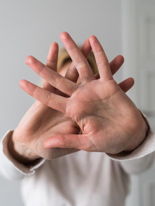 Eine Frau, deren Gesicht nicht zu erkennen ist, verschränkt ihre Hände und hält sie Richtung Kamera