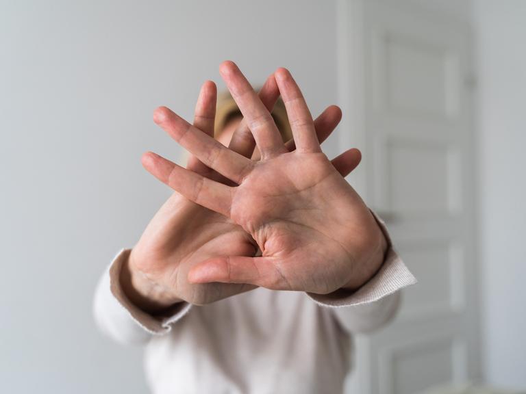 Eine Frau, deren Gesicht nicht zu erkennen ist, verschränkt ihre Hände und hält sie Richtung Kamera