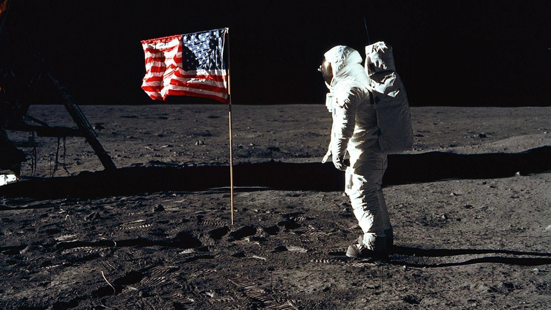 Ein Astronaut steht neben einer USA-Flagge auf dem Mond.