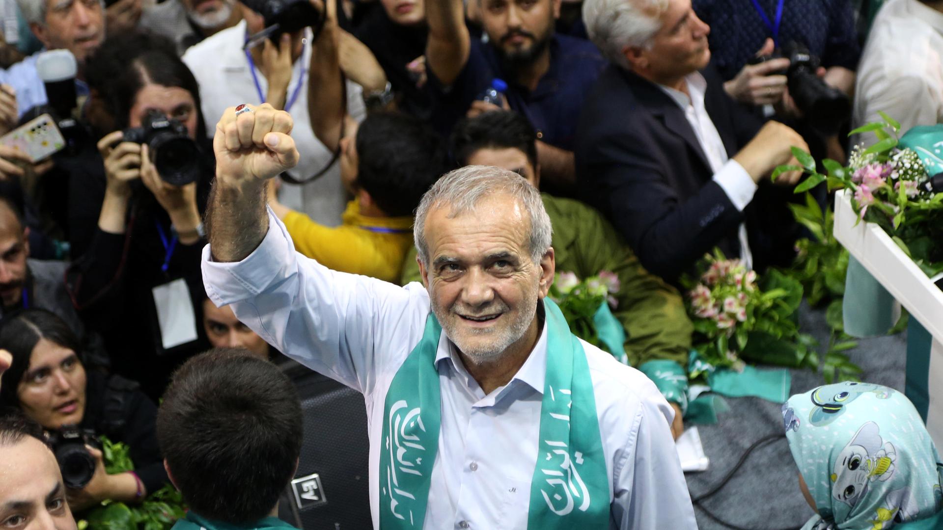 Der iranische Präsidentschaftskandidat Masoud Pezeshkian bei einer Wahlkampfveranstaltung in Teheran. Er streckt die rechte Faust in die Luft und lächelt umringt von Menschen nach oben in die Kamera.