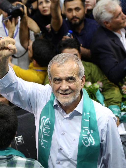 Der iranische Präsidentschaftskandidat Masoud Pezeshkian bei einer Wahlkampfveranstaltung in Teheran. Er streckt die rechte Faust in die Luft und lächelt umringt von Menschen nach oben in die Kamera.