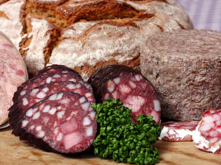 Auf dem Bild ist eine Brotzeit mit verschiedenen Wurstsorten und einem Laib Brot zu sehen.