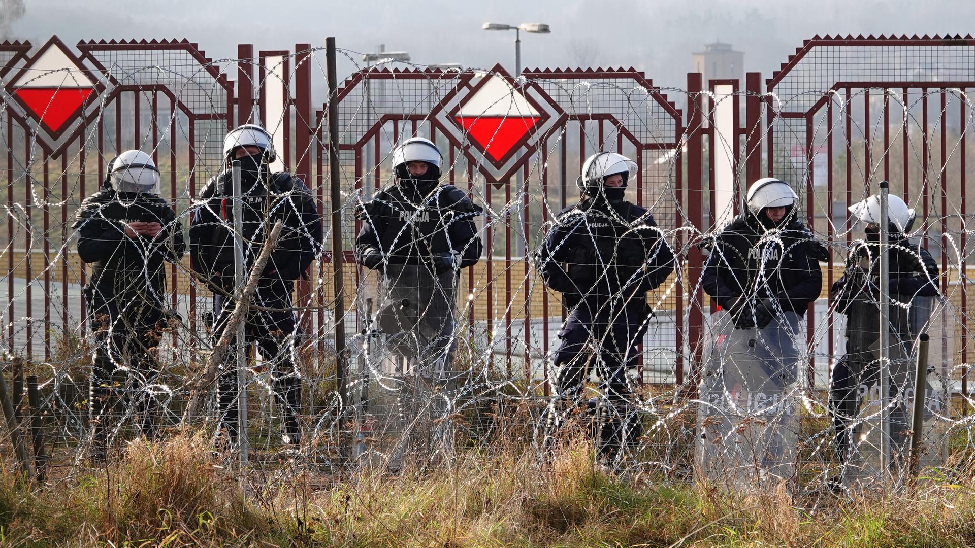 Polnische Sicherheitskräfte stehen an der Grenze hinter Stacheldraht.