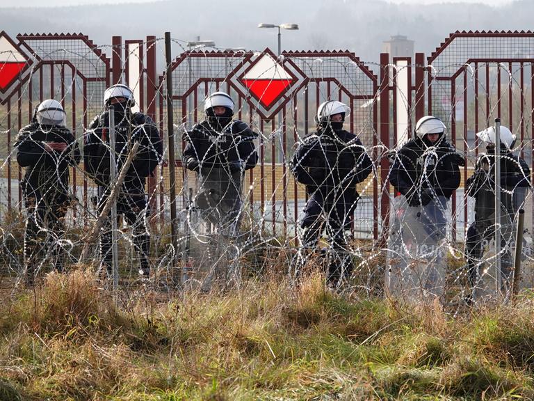 Polnische Sicherheitskräfte stehen an der Grenze hinter Stacheldraht.