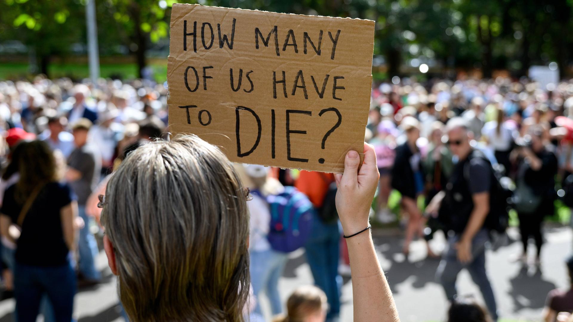 Eine Frau hält ein Pappschild, auf dem steht: "How many of us have to die?" Im Hintergrund sieht man Demo-Teilnehmer.