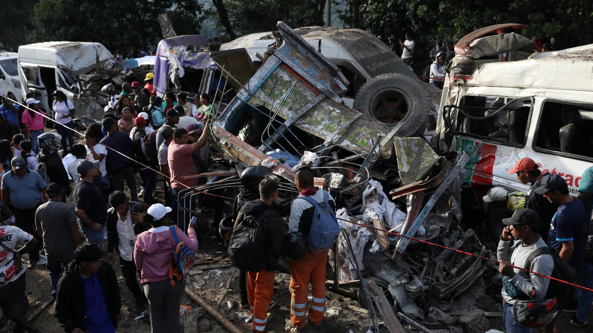 Menschen stehen zwischen zerbeulten und ausgebrannten Autos. 