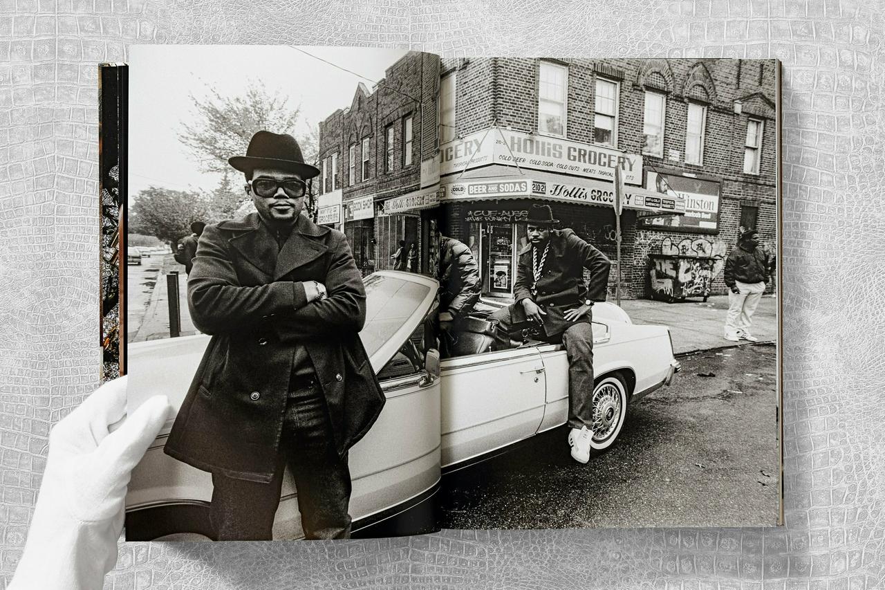 Eine aufgeschlagene Seite aus dem Buch "Ice Cold. A Hip-Hop Jewelry History" zeigt die Rapper von Run DMC posierend vor einem Auto.