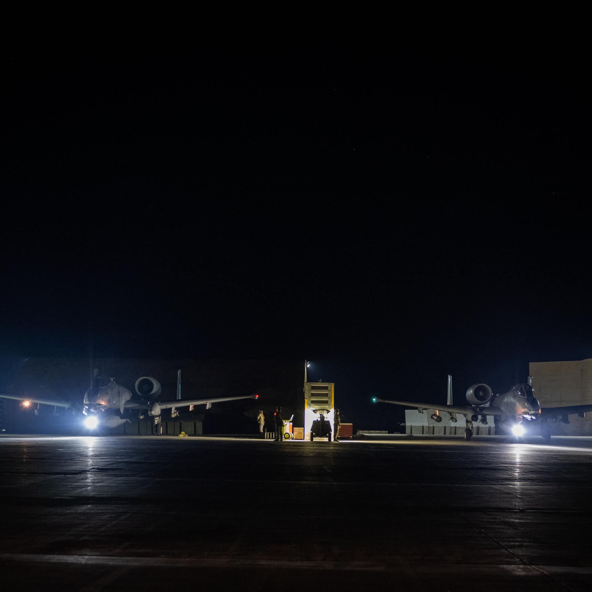 Auf einem Flugplatz stehen in der Nacht zwei spärlich beleuchtete Flugzeuge.