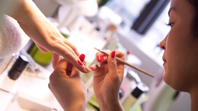 Eine Hand mit rot lackierten Fingernägeln, die von einer anderen Hand gehalten wird.