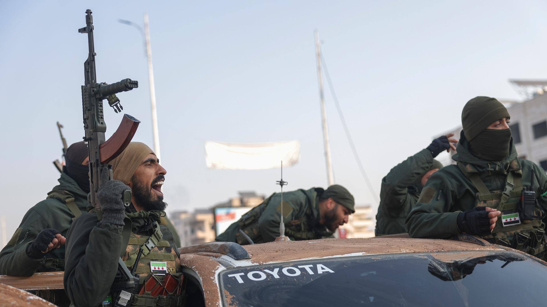 Mehrere syrische Kämpfer stehen auf einem Geländewagen. Einer hält in der rechten Hand ein Maschinengewehr.