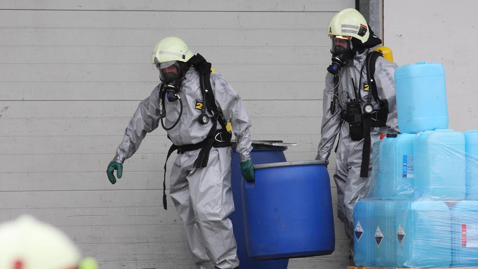 Feuerwehrleute in Schutzanzügen räumen giftige Stoffe in Tonnen aus einem Lager in Urmitz, Rheinland-Pfalz.