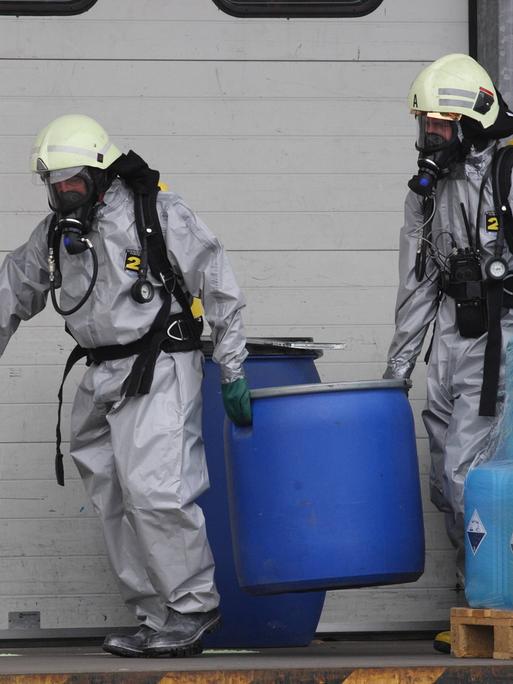 Feuerwehrleute in Schutzanzügen räumen giftige Stoffe in Tonnen aus einem Lager in Urmitz, Rheinland-Pfalz.