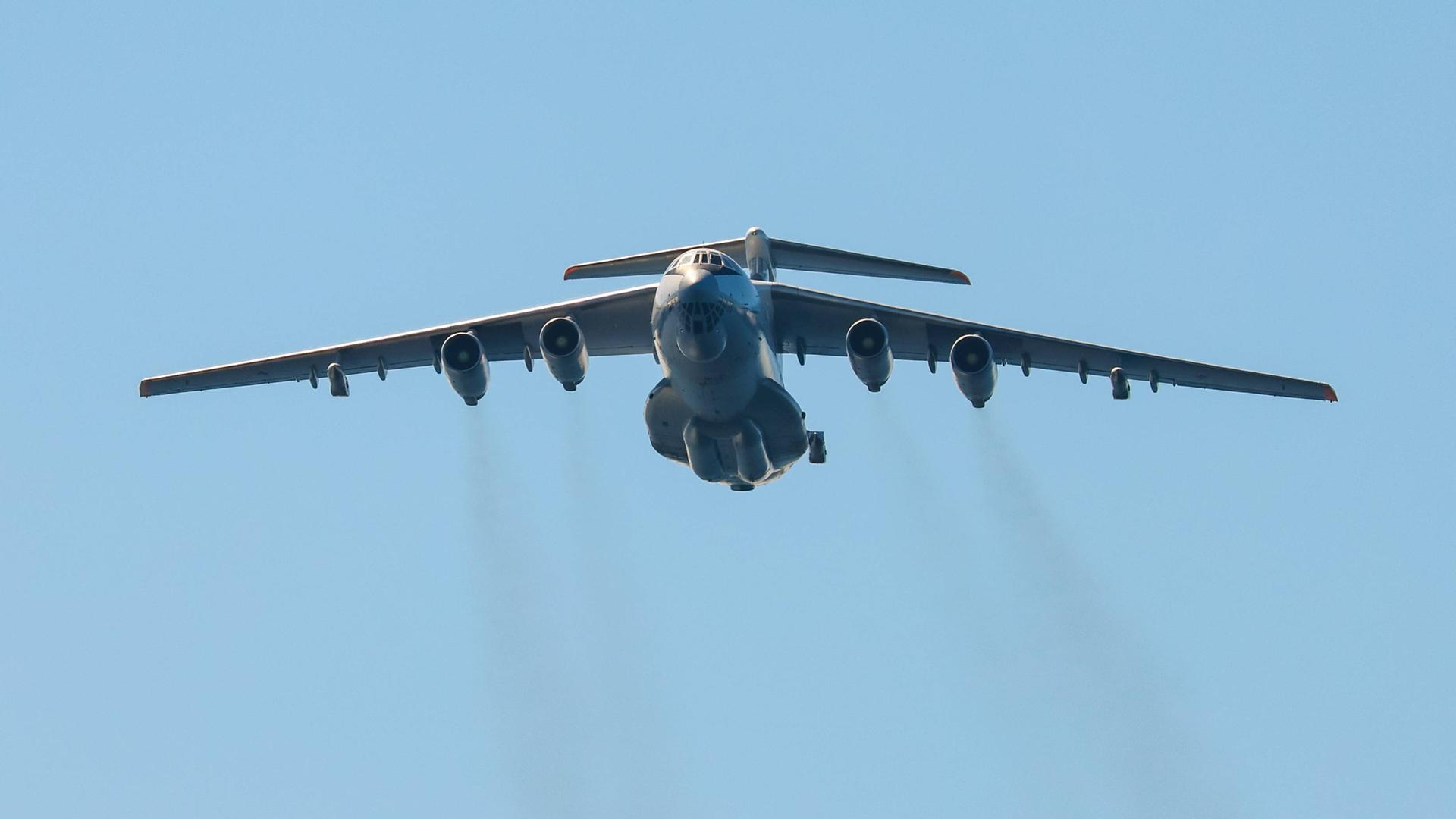 Das Bild zeigt eine große Militärmaschine am Himmel. Aus den insgesamt vier Düsen strömen dunkle Abgase.