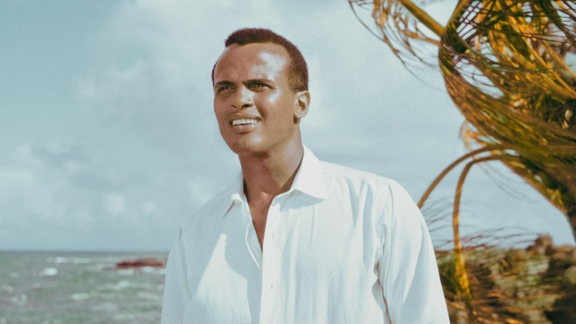 Der amerikanische Schauspieler und Sänger Harry Belafonte posiert um 1957 unter einer Palme mit Blick aufs Meer. 