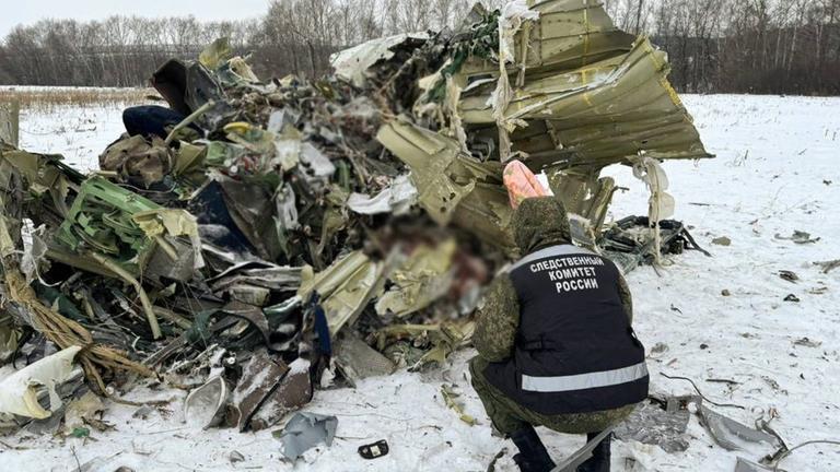 Eine Person kniet vor einem Teil von dem zerstörten Flugzeug.
