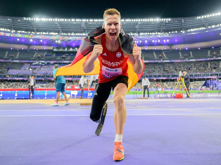 Markus Rehm aus Deutschland feiert seine Goldmedaille. Er hat die Deutschlandfahne um die Schulter gelegt und ballt die Fäuste in Richtung Kamera.