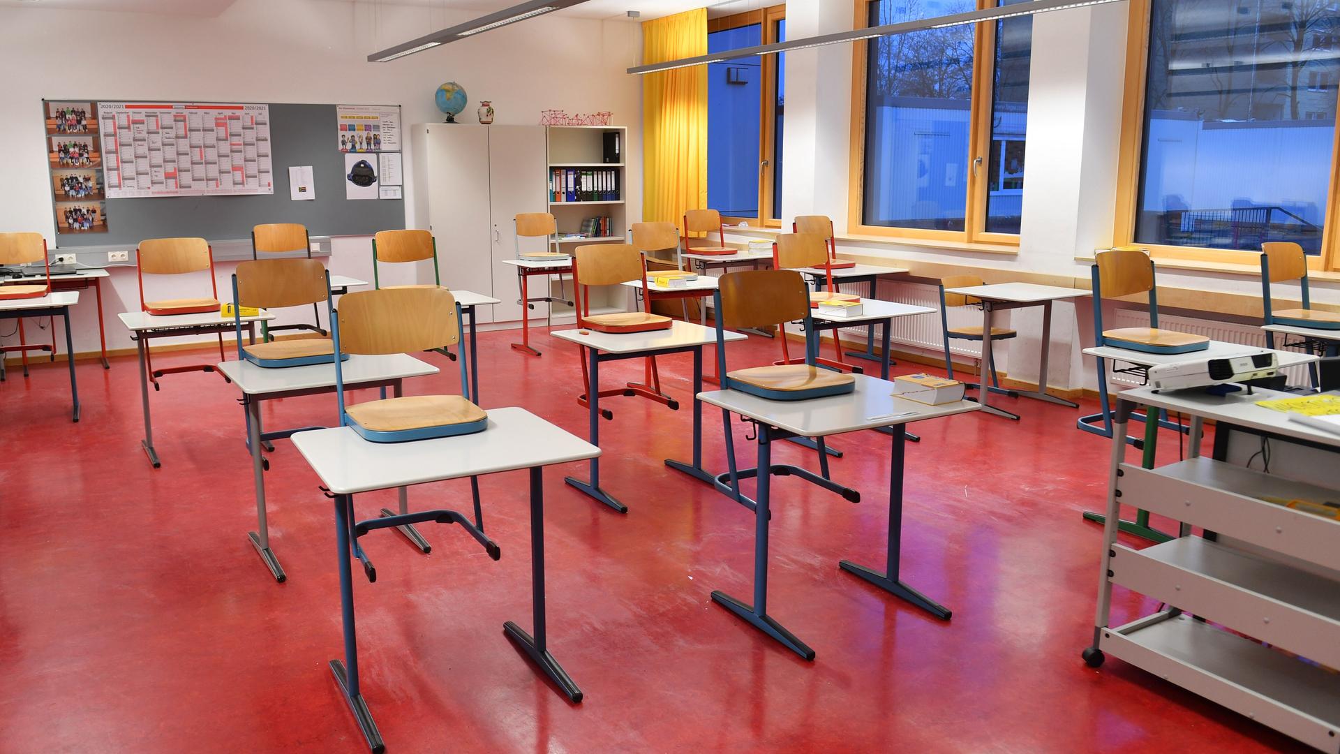 Ein leeres Klassenzimmer mit rotem Linolboden, in dem die Stühle auf die Tische gestellt sind. 