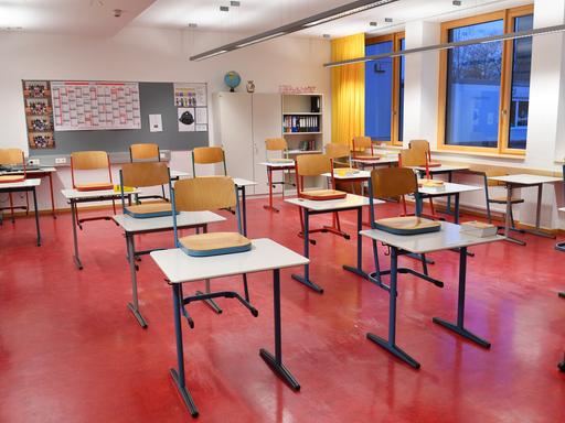 Ein leeres Klassenzimmer mit rotem Linolboden, in dem die Stühle auf die Tische gestellt sind. 