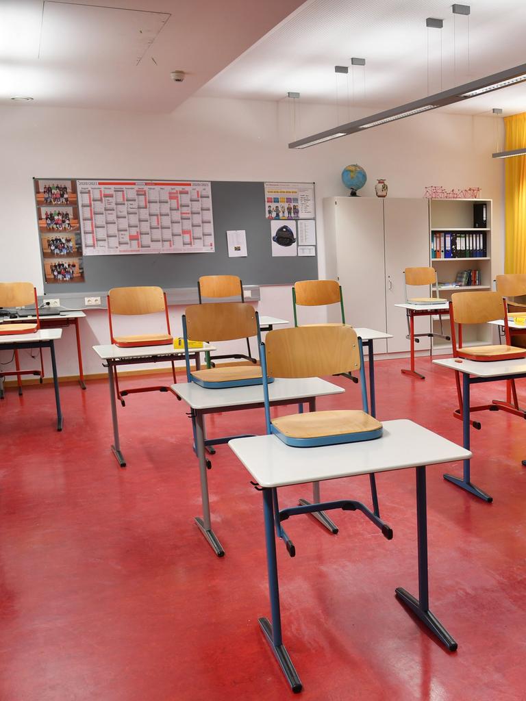 Ein leeres Klassenzimmer mit rotem Linolboden, in dem die Stühle auf die Tische gestellt sind. 