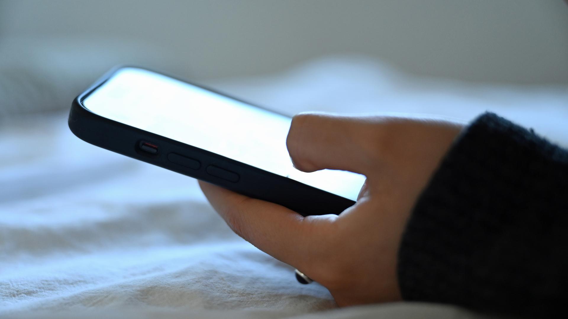 Eine junge Frau liegt mit dem Smartphone in der Hand auf dem Bett.