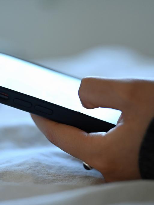 Eine junge Frau liegt mit dem Smartphone in der Hand auf dem Bett. Eine junge Frau liegt mit dem Smartphone in der Hand auf dem Bett.