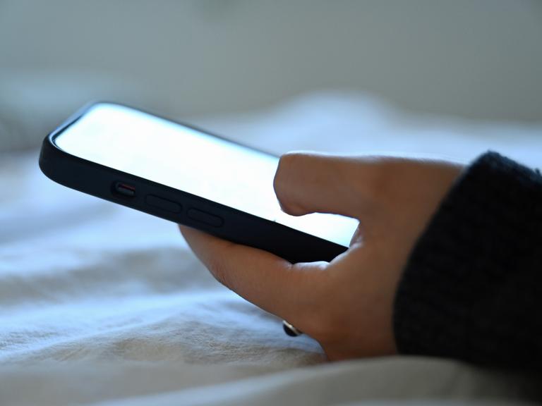 Eine junge Frau liegt mit dem Smartphone in der Hand auf dem Bett. Eine junge Frau liegt mit dem Smartphone in der Hand auf dem Bett.
