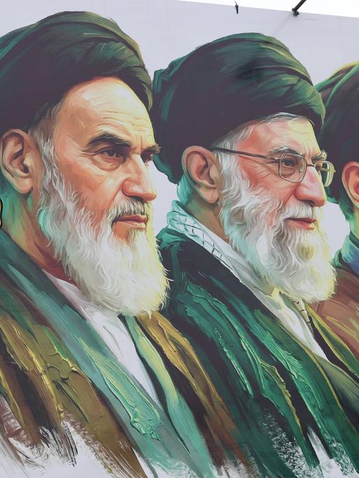 Ein Mann säubert ein Plakat auf dem v.l. Ayatollah Ruhollah Chomeini, Ali Chamenei und Modschtaba Chamenei zu sehen sind.