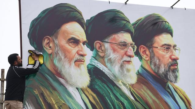 Ein Mann säubert ein Plakat auf dem v.l. Ayatollah Ruhollah Chomeini, Ali Chamenei und Modschtaba Chamenei zu sehen sind.