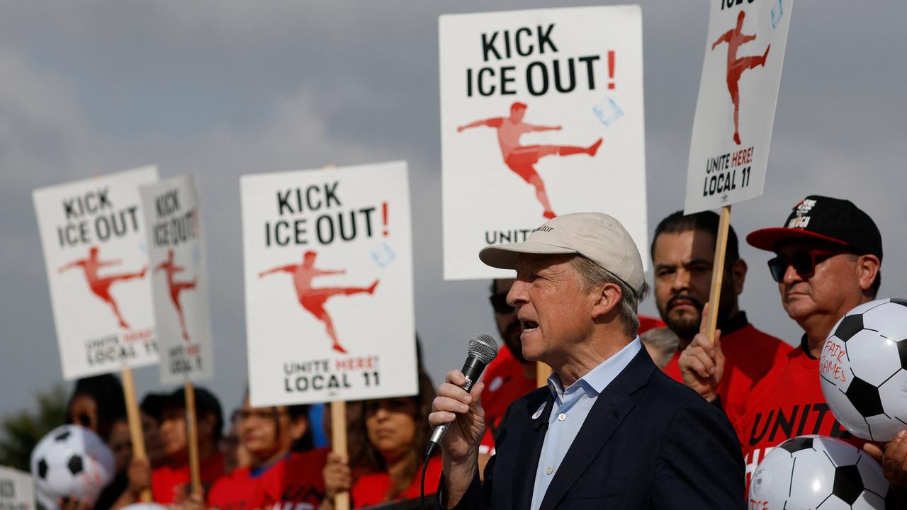 Zu sehen sind ein Redner mit Mikrofon und Protestierende in roter Kleidung. Sie halten Schilder mit der Aufschrift hoch: "Kick ICE out"