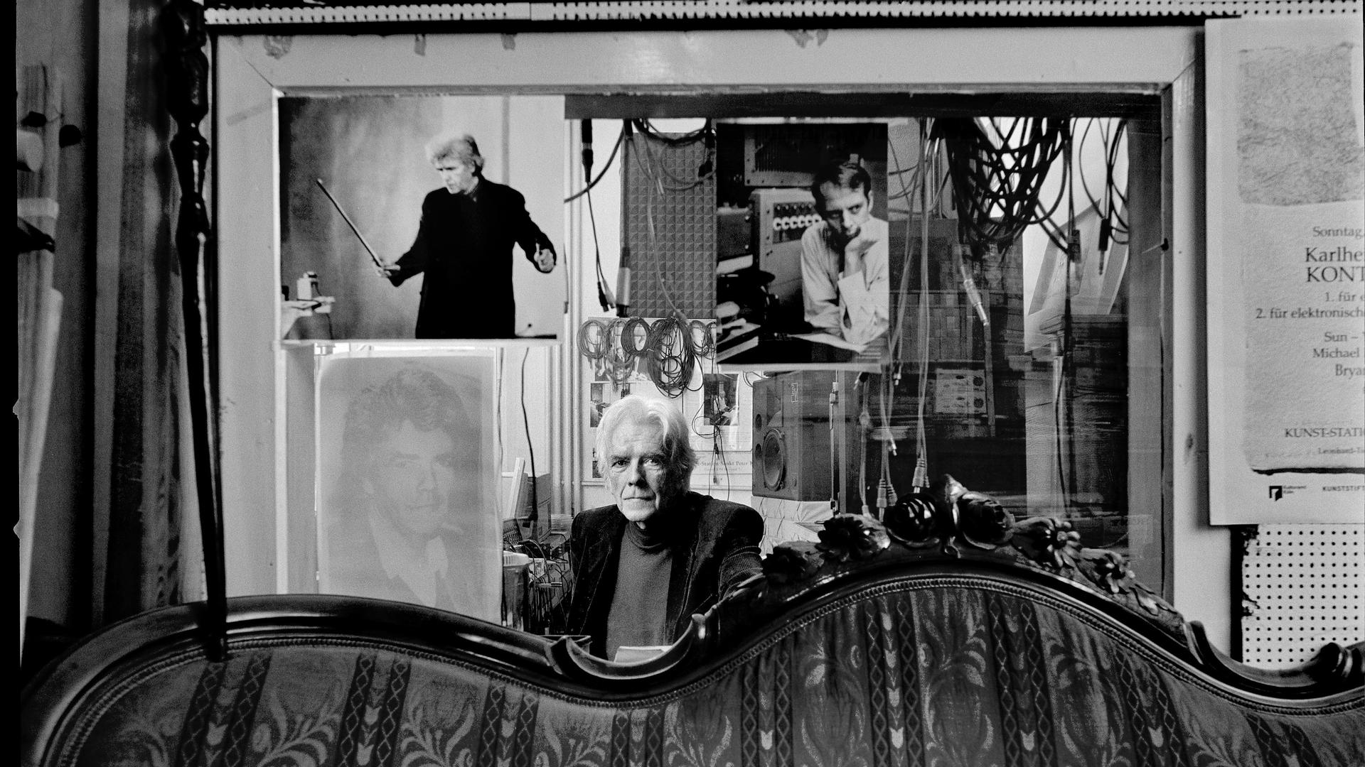 Der Komponist Johannes Fritsch sitzt hinter einem antiquierten Sofa in seinem Studio in Köln vor einer Glassscheibe, die das Studio vom Regieraum abtrennt