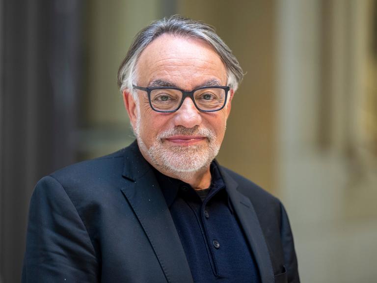 Natan Sznaider im Vorfeld einer Veranstaltung. Er lächelt zurückhaltend, der Hintergrund ist unscharf. Er trägt eine Brille mit dunklem Rand und ein dunkelblaues Sakko. 