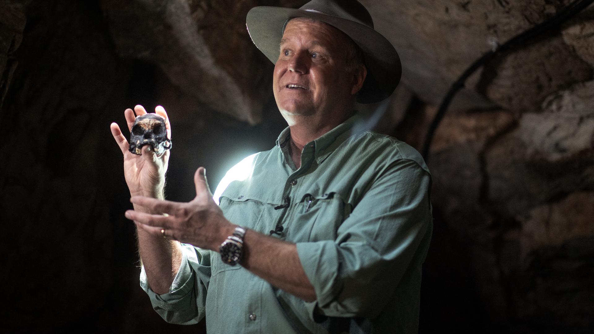 Ein Mann in einer Höhle hält einen kleinen menschenähnlichen Schädel in den Händen. Ein Mann in einer Höhle hält einen kleinen menschenähnlichen Schädel in den Händen.