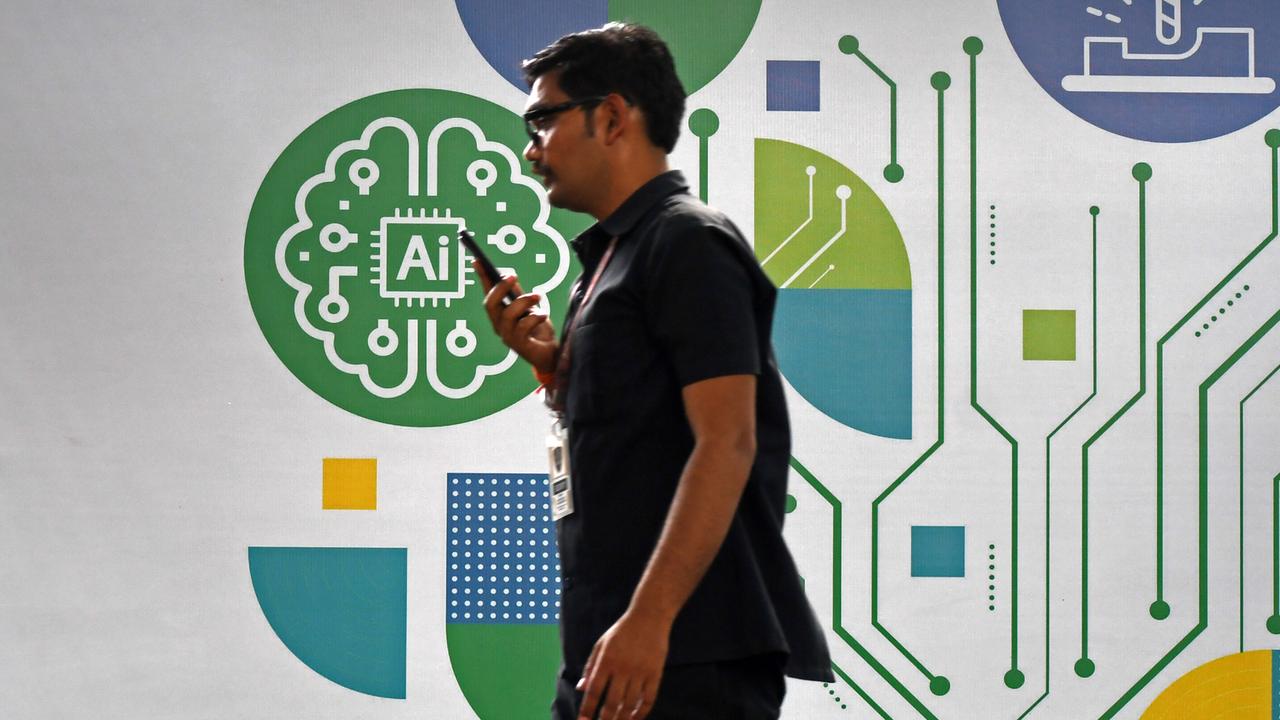 Ein Mann schaut auf sein Handy, während er an einem Plakat zum Thema Künstliche Intelligenz (KI/AI) auf einer Messe vorbeigeht.