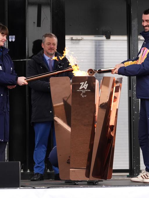 Eine Frau und ein Mann halten eine Fackel in ein Feuer. 