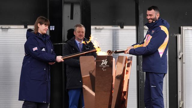 Eine Frau und ein Mann halten eine Fackel in ein Feuer. 