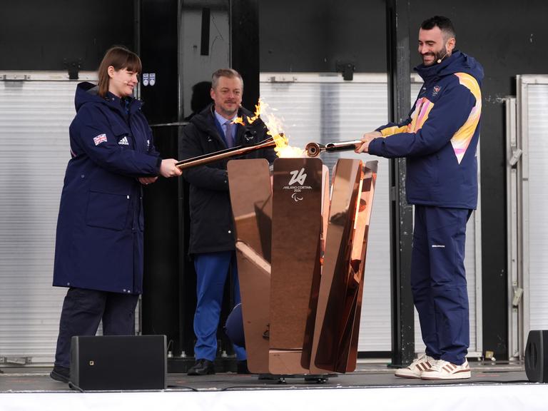 Eine Frau und ein Mann halten eine Fackel in ein Feuer. 