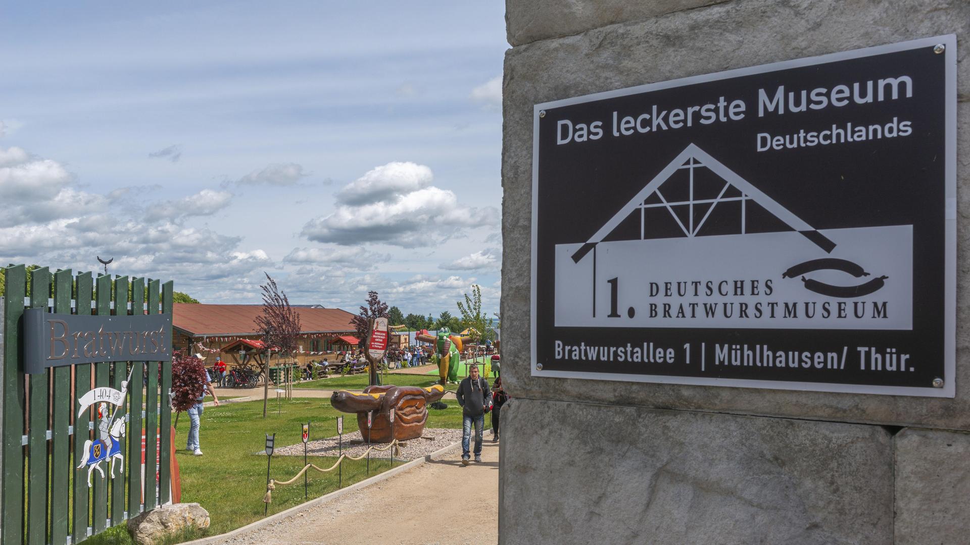 Eingang des ersten Deutschen Bratwurstmuseums in Mühlhausen mit Inschrift und einer mittelalterlichen Ritterfigur mit der Jahreszahl 1404. Museumsgelände im Freien mit einer riesigen Thüringer Bratwurst in Brot mit Senf in Thüringen. Eingang des ersten Deutschen Bratwurstmuseums in Mühlhausen mit Inschrift und einer mittelalterlichen Ritterfigur mit der Jahreszahl 1404. Museumsgelände im Freien mit einer riesigen Thüringer Bratwurst in Brot mit Senf in Thüringen.