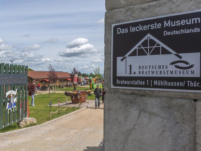 Eingang des ersten Deutschen Bratwurstmuseums in Mühlhausen mit Inschrift und einer mittelalterlichen Ritterfigur mit der Jahreszahl 1404. Museumsgelände im Freien mit einer riesigen Thüringer Bratwurst in Brot mit Senf in Thüringen.