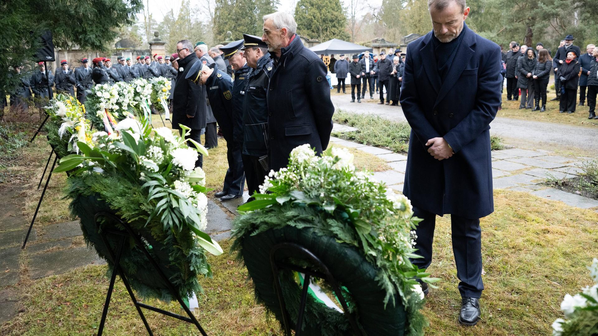 Armin Schuster (CDU, M), Innenminister von Sachsen, und Jörg Scheibe (BSW, r), Vizepräsident des Sächsischen Landtages, stehen während einer Gedenkveranstaltung auf dem Nordfriedhof vor einem Blumenkranz.
